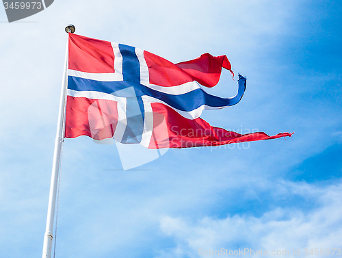 Image of The Royal flag of Norway on a pole towards blue and white sky in