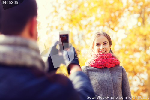 Image of smiling couple with smartphone in autumn park