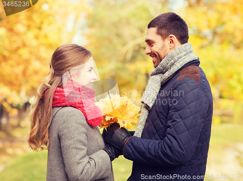 Image of smiling couple with bunch of leaves in autumn park