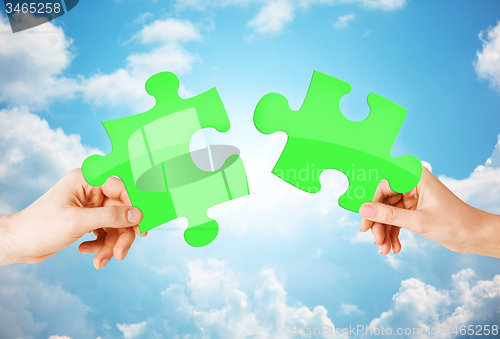 Image of hands with green puzzle over sky background