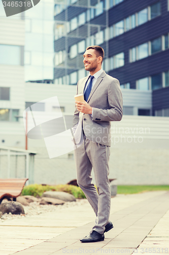 Image of young serious businessman with paper cup outdoors