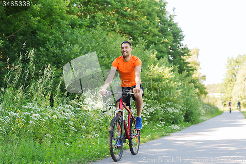 Image of happy young man riding bicycle outdoors