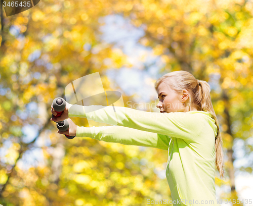 Image of sporty woman with light dumbbells outdoors