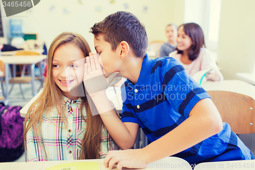 Image of smiling schoolboy whispering to classmate ear