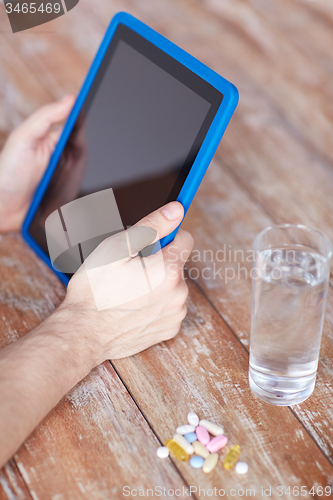 Image of close up of hands with tablet pc, pills and water