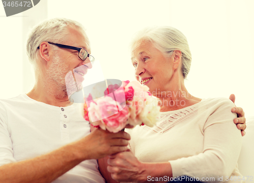 Image of happy senior couple with bunch of flowers at home