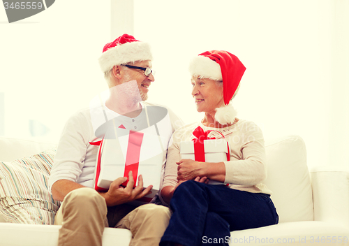 Image of happy senior couple in santa hats with gift boxes