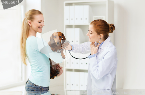 Image of happy woman with dog and doctor at vet clinic