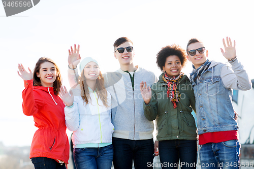 Image of happy teenage friends waving hands on city street