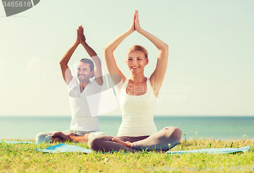 Image of smiling couple making yoga exercises outdoors