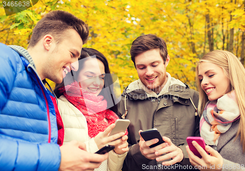 Image of smiling friends with smartphones in city park