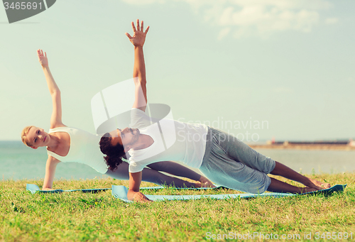 Image of smiling couple making yoga exercises outdoors