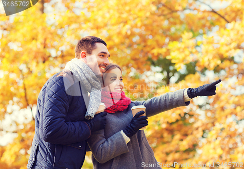 Image of smiling couple with coffee cups in autumn park