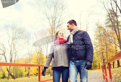 Image of smiling couple hugging on bridge in autumn park