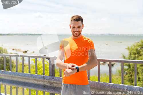 Image of smiling young man with smart wristwatch at seaside