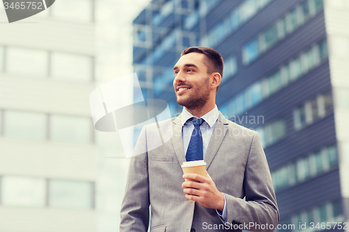 Image of young smiling businessman with paper cup outdoors