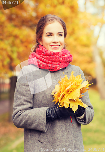 Image of smiling woman with bunch of leaves in autumn park