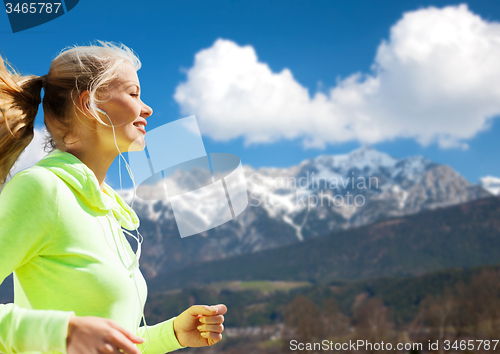 Image of happy young woman with earphones jogging outdoors