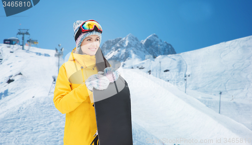 Image of happy young woman with snowboard over mountains