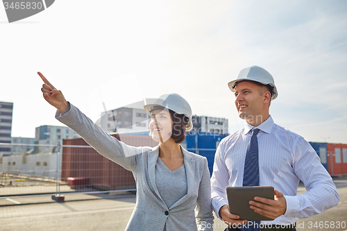 Image of happy builders in hardhats with tablet pc outdoors