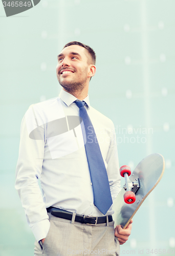 Image of young smiling businessman with skateboard outdoors