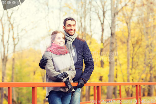 Image of smiling couple hugging on bridge in autumn park