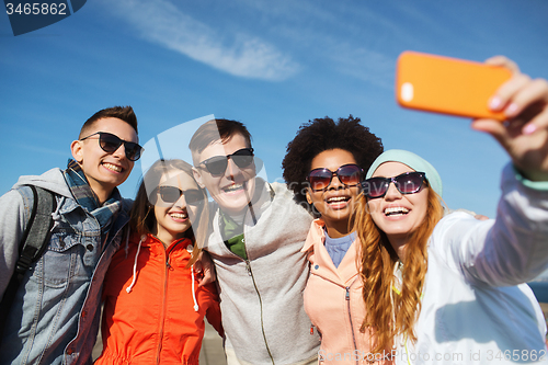 Image of smiling friends taking selfie with smartphone