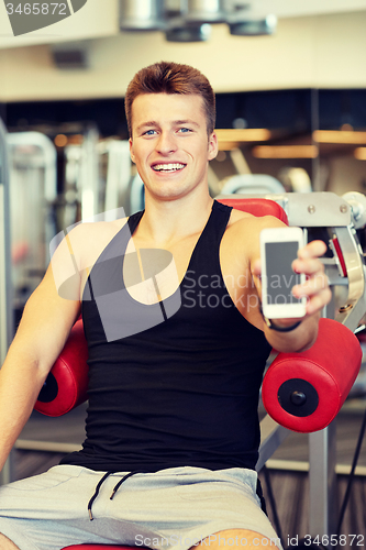 Image of smiling young man with smartphone in gym