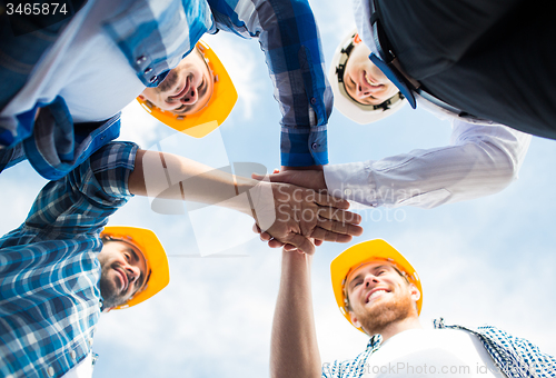 Image of close up of builders in hardhats with hands on top