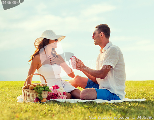 Image of smiling couple with small red gift box on picnic