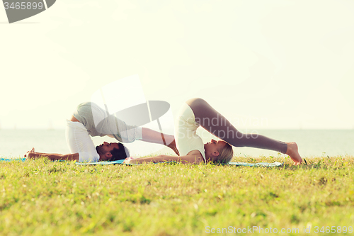 Image of smiling couple making yoga exercises outdoors