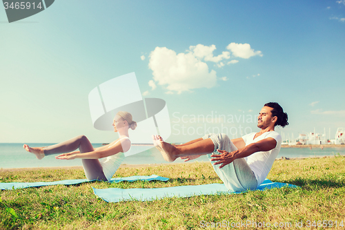 Image of smiling couple making yoga exercises outdoors