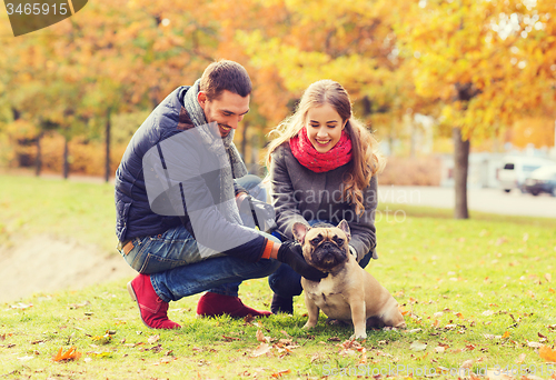 Image of smiling couple with dog in autumn park