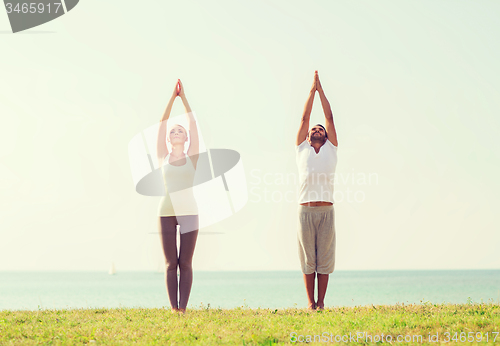 Image of smiling couple making yoga exercises outdoors