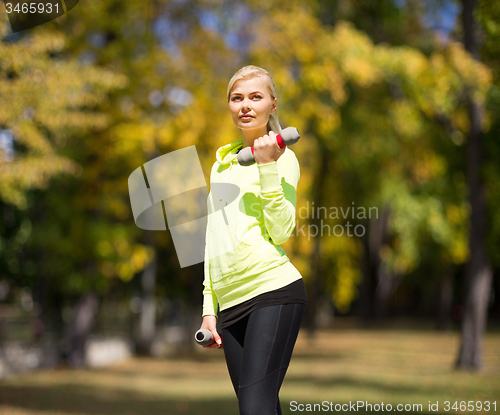 Image of sporty woman with light dumbbells outdoors