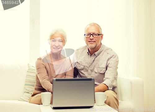 Image of happy senior couple with laptop and cups at home