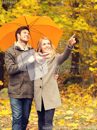 Image of smiling couple with umbrella in autumn park