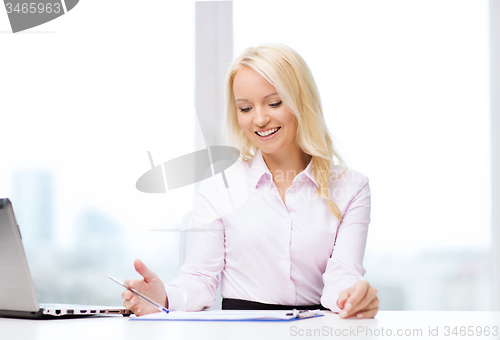 Image of smiling businesswoman reading papers in office