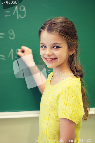Image of little smiling schoolgirl writing on chalk board