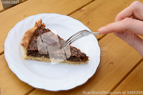 Image of Woman uses dessert fork to cut into a slice of pecan pie