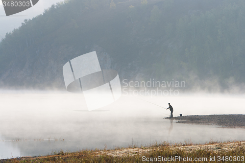 Image of Man fishing at river shore 