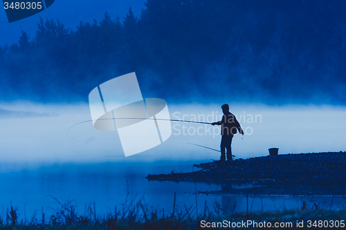 Image of Man fishing at river shore 