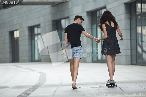 Image of Young pair in love of stylish teenagers ride longboards 