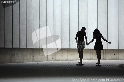 Image of Young pair in love of stylish teenagers ride longboards 