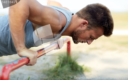 Image of young man exercising on horizontal bar outdoors