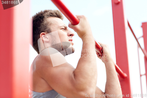 Image of young man exercising on horizontal bar outdoors