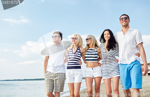 Image of smiling friends in sunglasses walking on beach