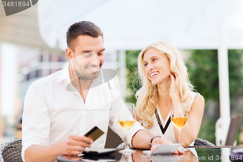 Image of happy couple with bank card and bill at restaurant