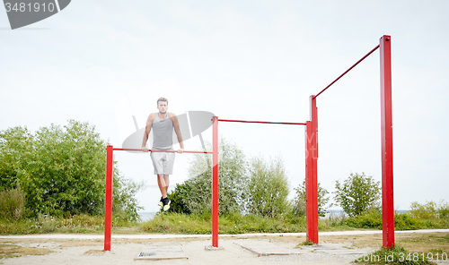 Image of young man exercising on horizontal bar outdoors