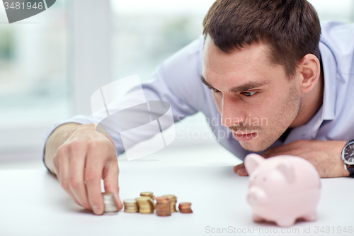 Image of businessman with piggy bank and coins at office